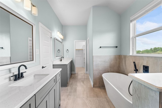 bathroom with a bath, vanity, vaulted ceiling, and tile walls