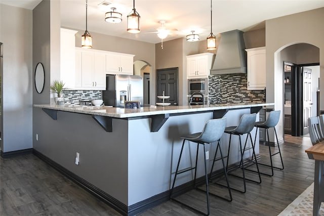 kitchen with white cabinetry, hanging light fixtures, stainless steel appliances, premium range hood, and a kitchen bar