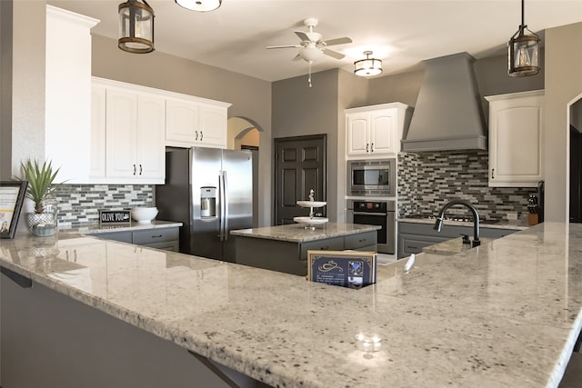 kitchen featuring custom exhaust hood, a center island, appliances with stainless steel finishes, light stone counters, and white cabinetry