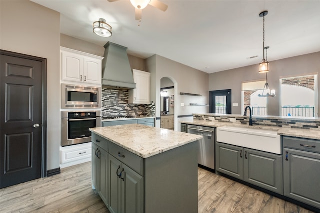 kitchen featuring custom range hood, stainless steel appliances, a kitchen island, gray cabinets, and white cabinetry