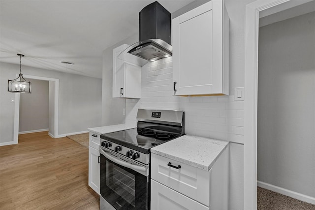 kitchen with white cabinetry, hanging light fixtures, wall chimney range hood, light stone counters, and stainless steel range oven