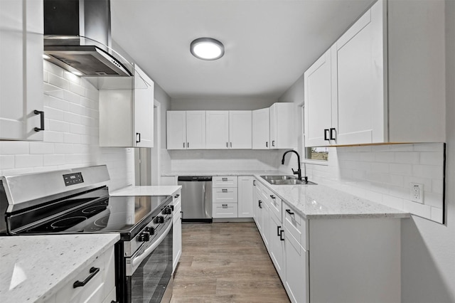 kitchen with sink, stainless steel appliances, wall chimney range hood, light stone counters, and white cabinets