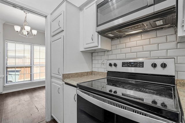 kitchen with white cabinets, ornamental molding, appliances with stainless steel finishes, wood-type flooring, and a chandelier