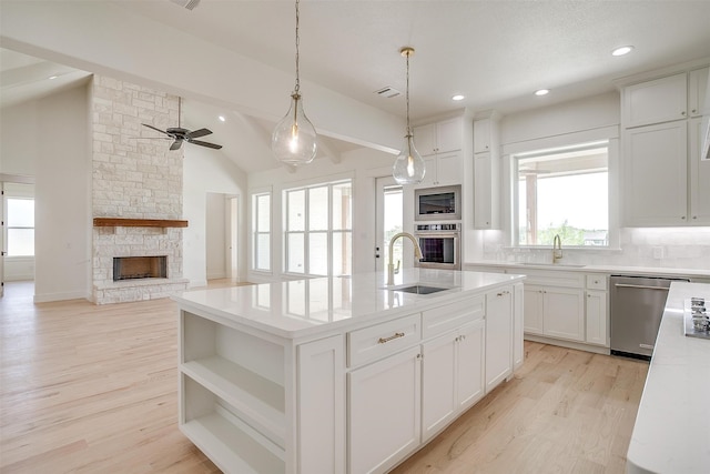 kitchen featuring a kitchen island with sink, stainless steel appliances, ceiling fan, a stone fireplace, and vaulted ceiling