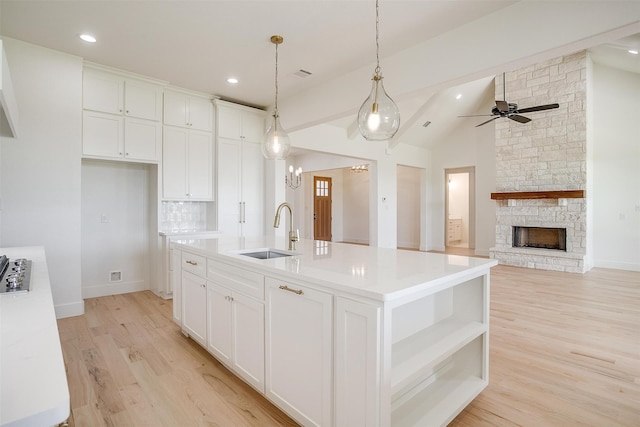 kitchen with white cabinetry, lofted ceiling, a stone fireplace, ceiling fan, and a center island with sink