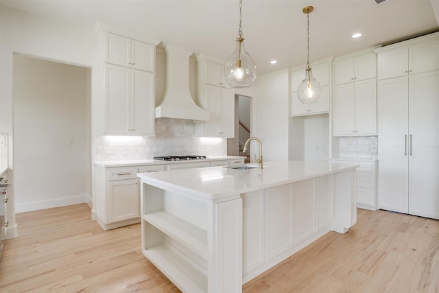 kitchen featuring an island with sink, custom range hood, light wood-type flooring, and white cabinets