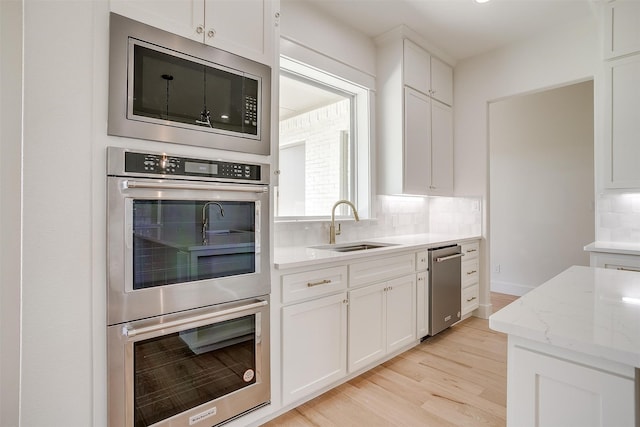 kitchen featuring white cabinetry, backsplash, stainless steel appliances, sink, and light hardwood / wood-style floors