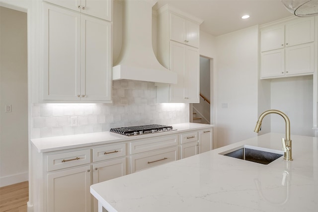 kitchen with custom range hood, light hardwood / wood-style flooring, light stone counters, sink, and stainless steel gas cooktop