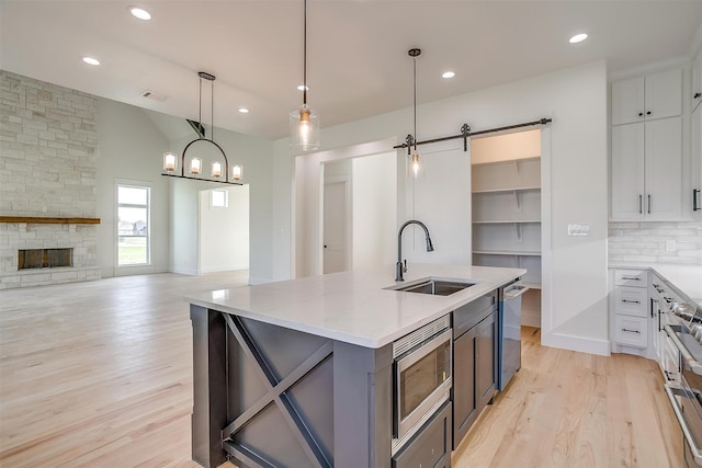 kitchen with appliances with stainless steel finishes, white cabinetry, sink, and light hardwood / wood-style flooring