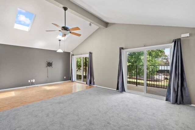 carpeted empty room featuring a skylight, ceiling fan, beamed ceiling, and high vaulted ceiling