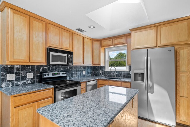 kitchen featuring a center island, sink, tasteful backsplash, light stone counters, and appliances with stainless steel finishes