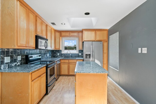 kitchen with a center island, light hardwood / wood-style flooring, a skylight, dark stone countertops, and appliances with stainless steel finishes