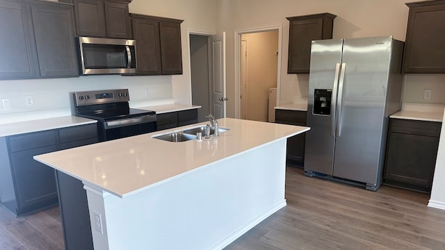 kitchen featuring sink, stainless steel appliances, dark brown cabinetry, light hardwood / wood-style flooring, and a center island with sink