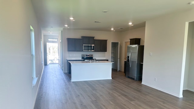 kitchen with appliances with stainless steel finishes, wood-type flooring, and an island with sink