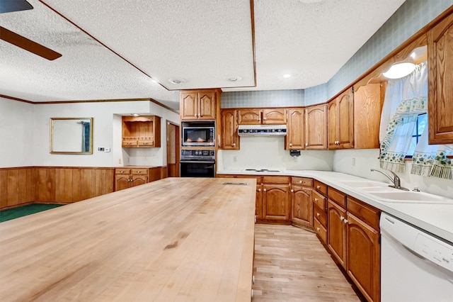 kitchen with dishwasher, wood walls, oven, sink, and built in microwave