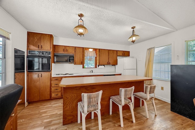 kitchen featuring pendant lighting, light hardwood / wood-style floors, tasteful backsplash, and black appliances