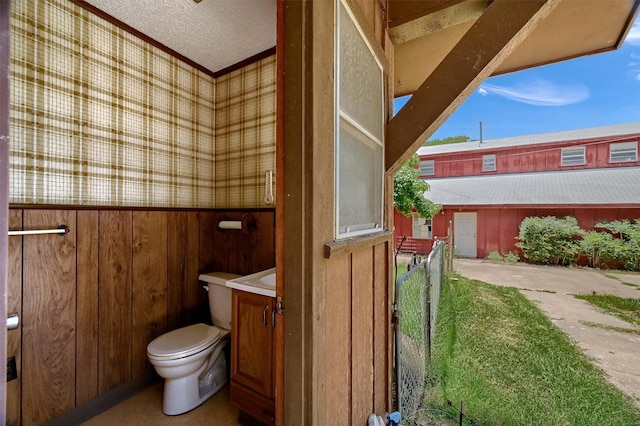 bathroom featuring a textured ceiling, toilet, and wood walls