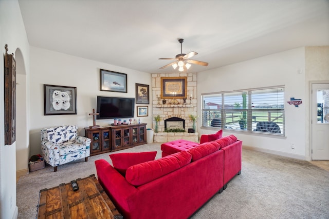 living room with a stone fireplace, carpet floors, and ceiling fan