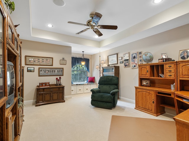 sitting room with a raised ceiling, light colored carpet, and ceiling fan