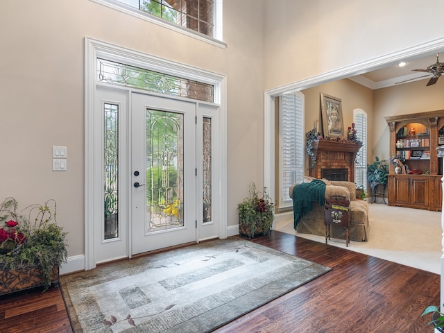 entryway featuring ceiling fan, ornamental molding, wood-type flooring, a brick fireplace, and a towering ceiling