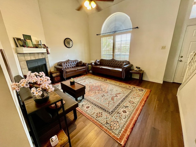 living room with a tile fireplace, ceiling fan, a towering ceiling, and dark hardwood / wood-style floors