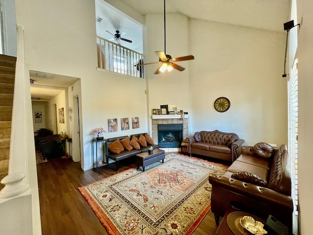 living room with dark hardwood / wood-style floors, ceiling fan, high vaulted ceiling, and a tiled fireplace