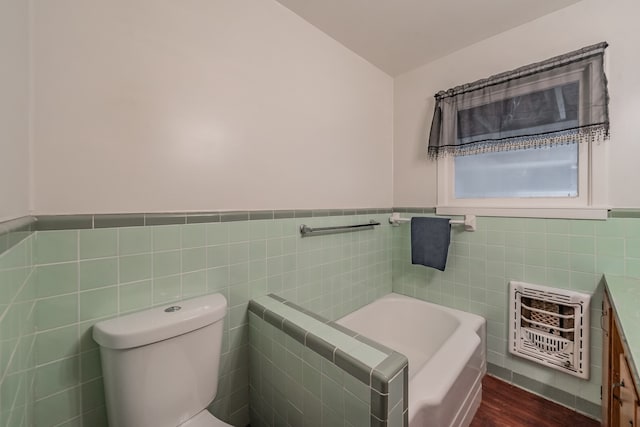 bathroom featuring vanity, a washtub, heating unit, tile walls, and toilet