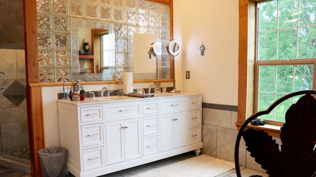 bathroom with tile patterned floors, a shower with door, dual bowl vanity, and tile walls