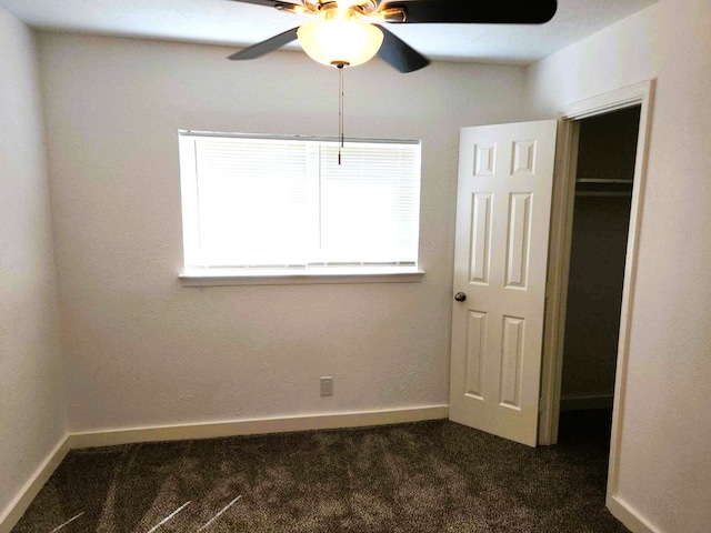 unfurnished bedroom with dark colored carpet, a closet, and ceiling fan