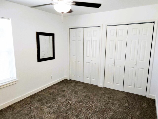 unfurnished bedroom featuring dark colored carpet, ceiling fan, and multiple closets