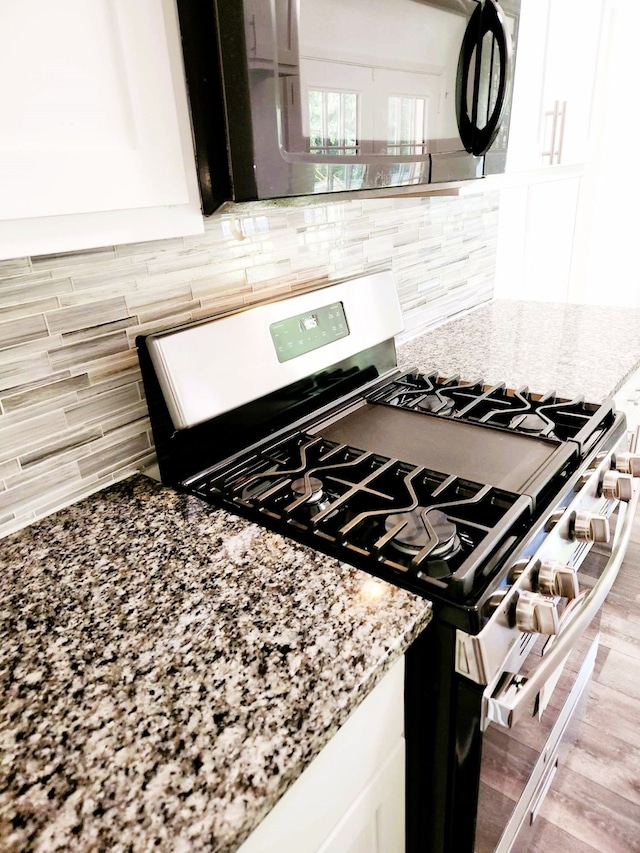 kitchen with stainless steel gas stove, light stone counters, backsplash, light hardwood / wood-style floors, and white cabinets