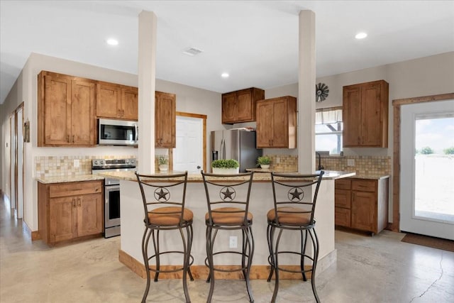 kitchen featuring appliances with stainless steel finishes, a breakfast bar, finished concrete floors, and brown cabinets