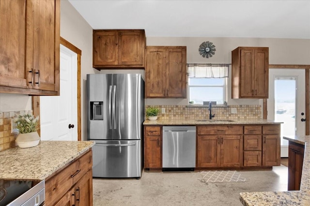 kitchen featuring decorative backsplash, brown cabinetry, light stone countertops, stainless steel appliances, and a sink