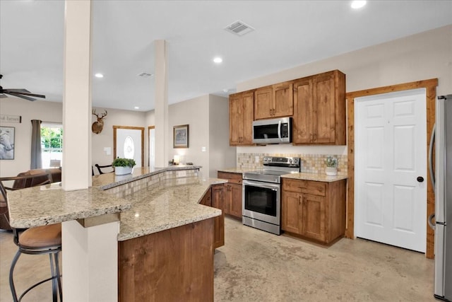 kitchen with a breakfast bar area, visible vents, appliances with stainless steel finishes, decorative backsplash, and brown cabinetry