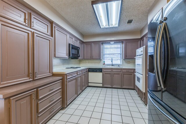 kitchen with light tile patterned floors, light countertops, visible vents, a sink, and white appliances