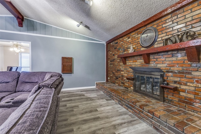 living area featuring vaulted ceiling with beams, a brick fireplace, a textured ceiling, wood finished floors, and baseboards