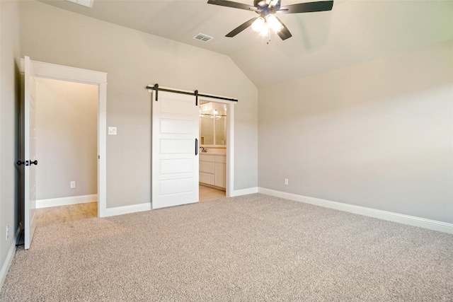 unfurnished bedroom with vaulted ceiling, connected bathroom, light colored carpet, ceiling fan, and a barn door