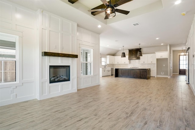 unfurnished living room with a tray ceiling, light hardwood / wood-style floors, a large fireplace, and ceiling fan