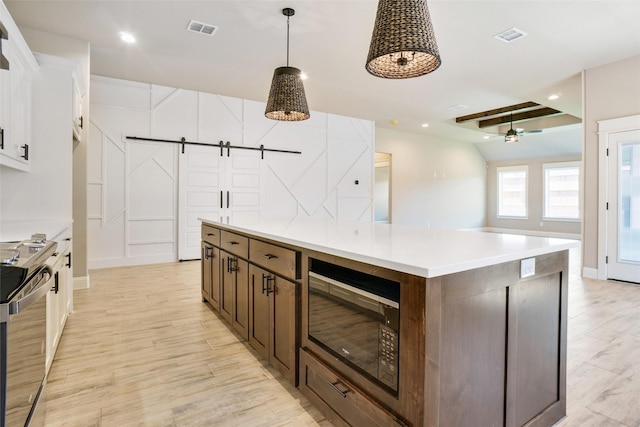 kitchen featuring stainless steel range with electric cooktop, decorative light fixtures, a center island, black microwave, and a barn door