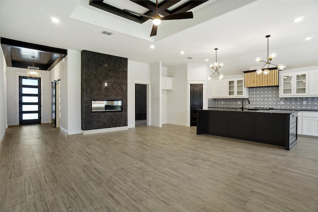 kitchen with hanging light fixtures, ceiling fan with notable chandelier, white cabinets, a raised ceiling, and a center island with sink