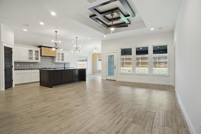 kitchen with tasteful backsplash, decorative light fixtures, ceiling fan with notable chandelier, an island with sink, and coffered ceiling