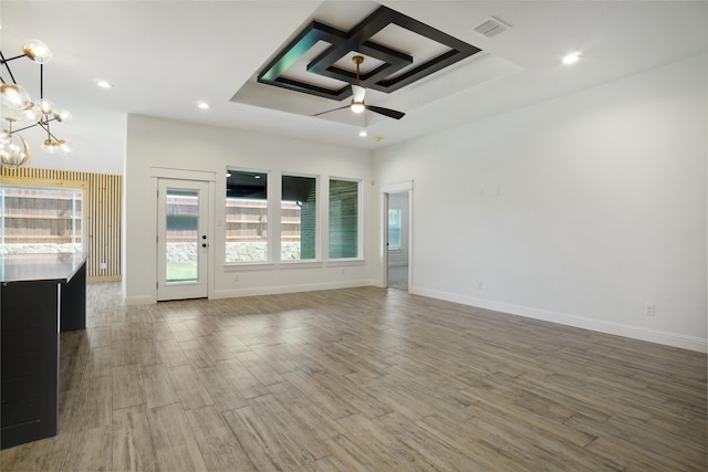 unfurnished living room with coffered ceiling, ceiling fan with notable chandelier, and hardwood / wood-style floors