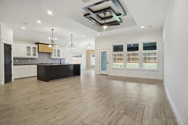 kitchen featuring backsplash, ceiling fan with notable chandelier, an island with sink, coffered ceiling, and pendant lighting