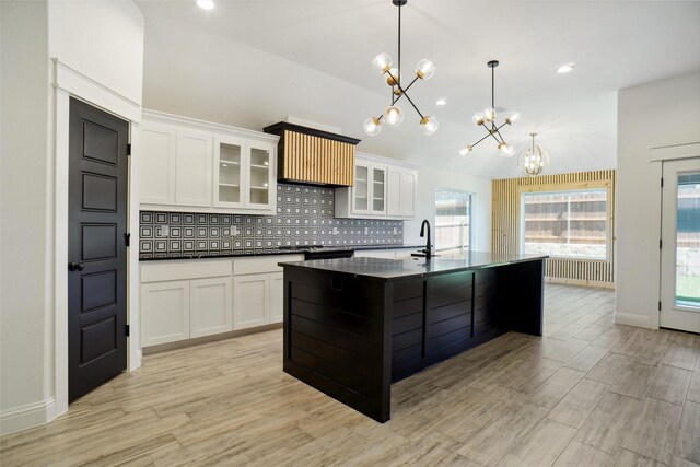 kitchen featuring pendant lighting, an island with sink, white cabinets, light hardwood / wood-style flooring, and backsplash