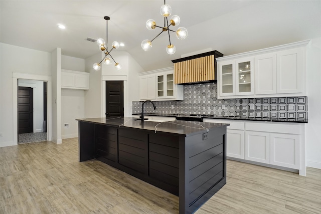 kitchen with light hardwood / wood-style flooring, white cabinets, tasteful backsplash, and an island with sink