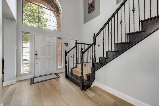 foyer entrance with a wealth of natural light, a towering ceiling, and light wood-type flooring