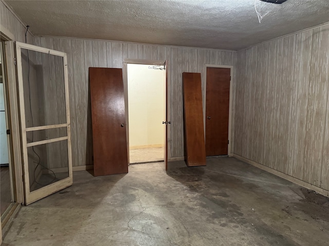 unfurnished bedroom with a textured ceiling, wooden walls, and concrete floors