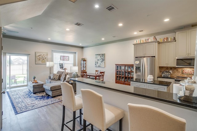 kitchen with light hardwood / wood-style flooring, backsplash, cream cabinets, appliances with stainless steel finishes, and ornamental molding