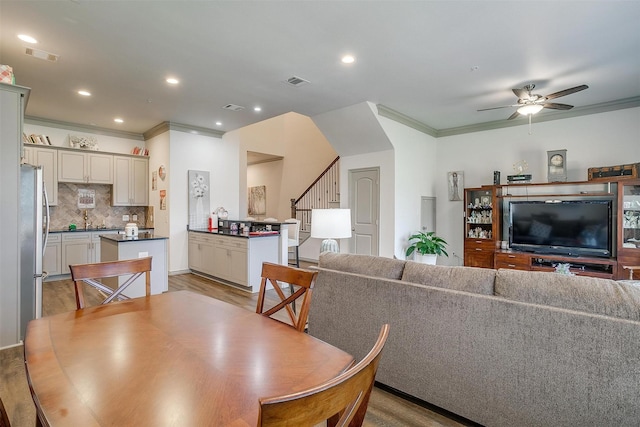 dining space with ceiling fan, light hardwood / wood-style floors, ornamental molding, and sink