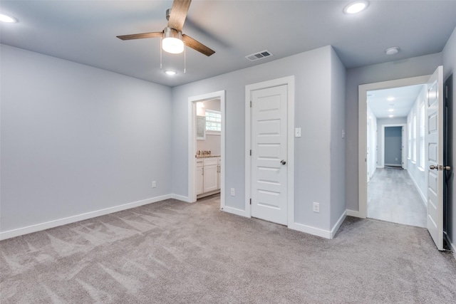 unfurnished bedroom with light carpet, connected bathroom, a closet, and ceiling fan